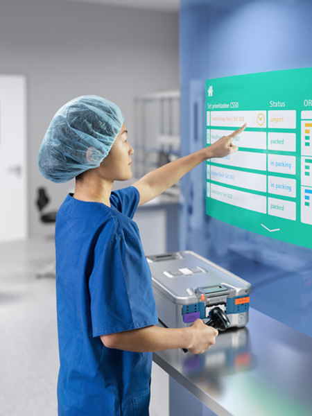 A female healthcare professional stands by a large screen, pointing to something on it