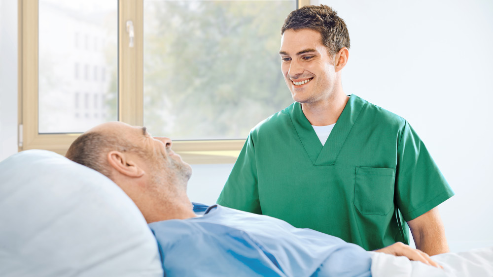 Un'infermiera parla con un paziente al letto