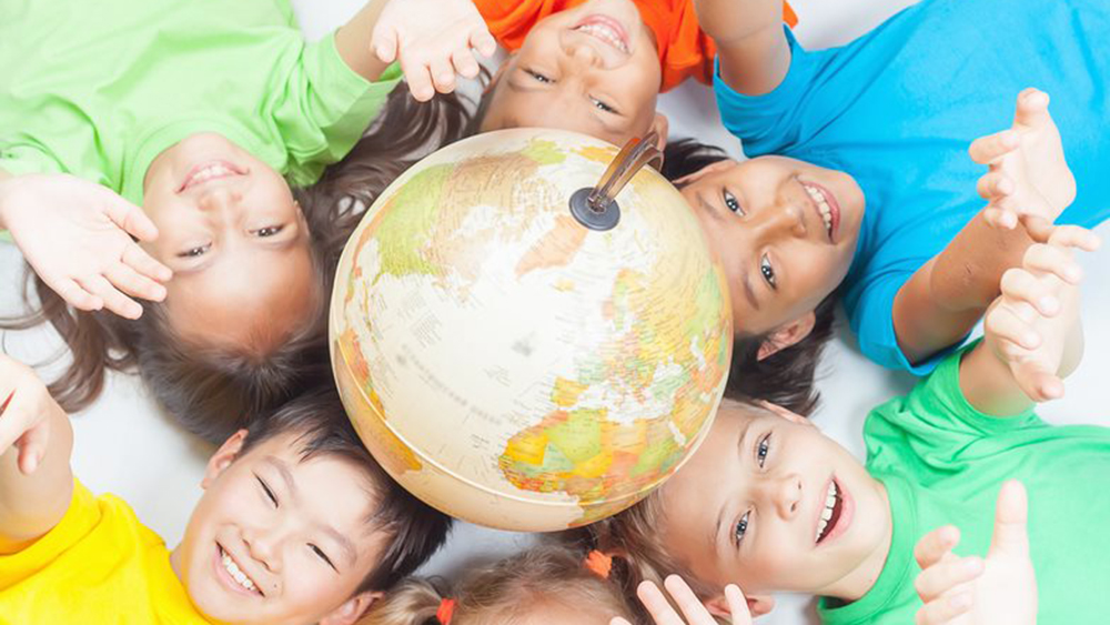 Bambini sorridenti sdraiati attorno a un mappamondo appoggiato a terra, con le braccia tese verso l’alto.